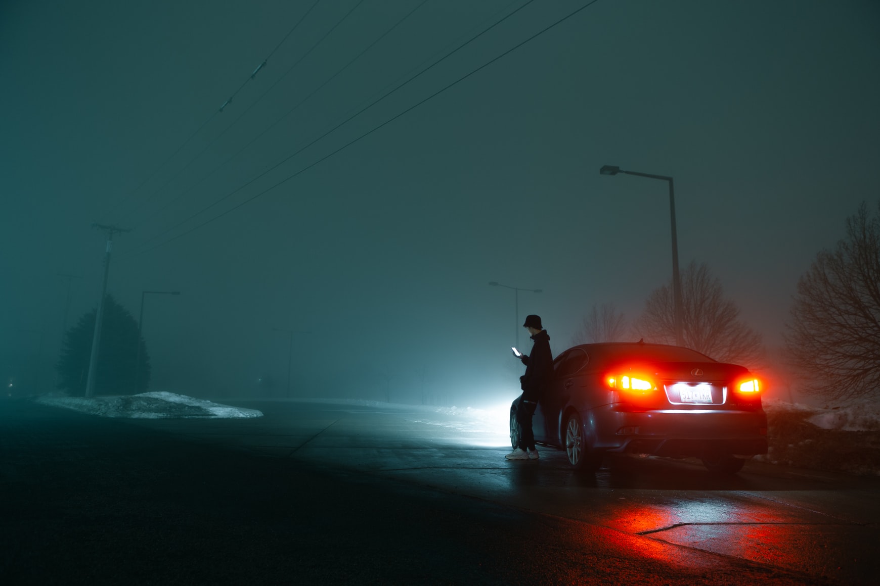 A driver standing outside of his broken down car on the side of the road at night