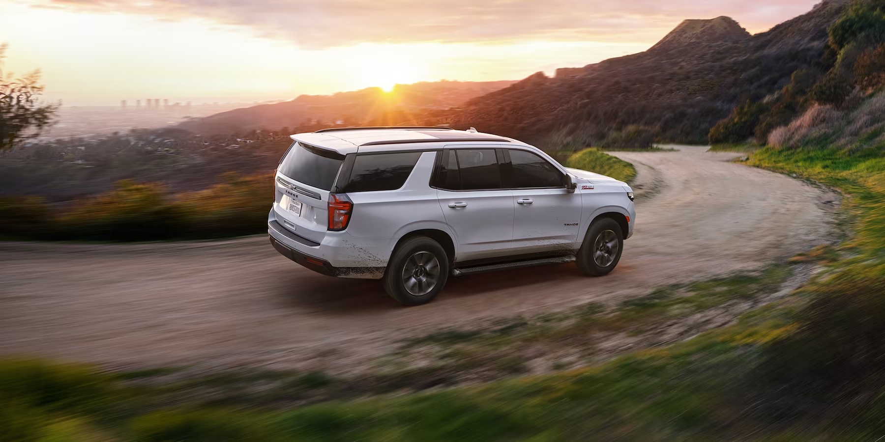 The 2022 Chevrolet Tahoe is driving through an open mountain road at sunset