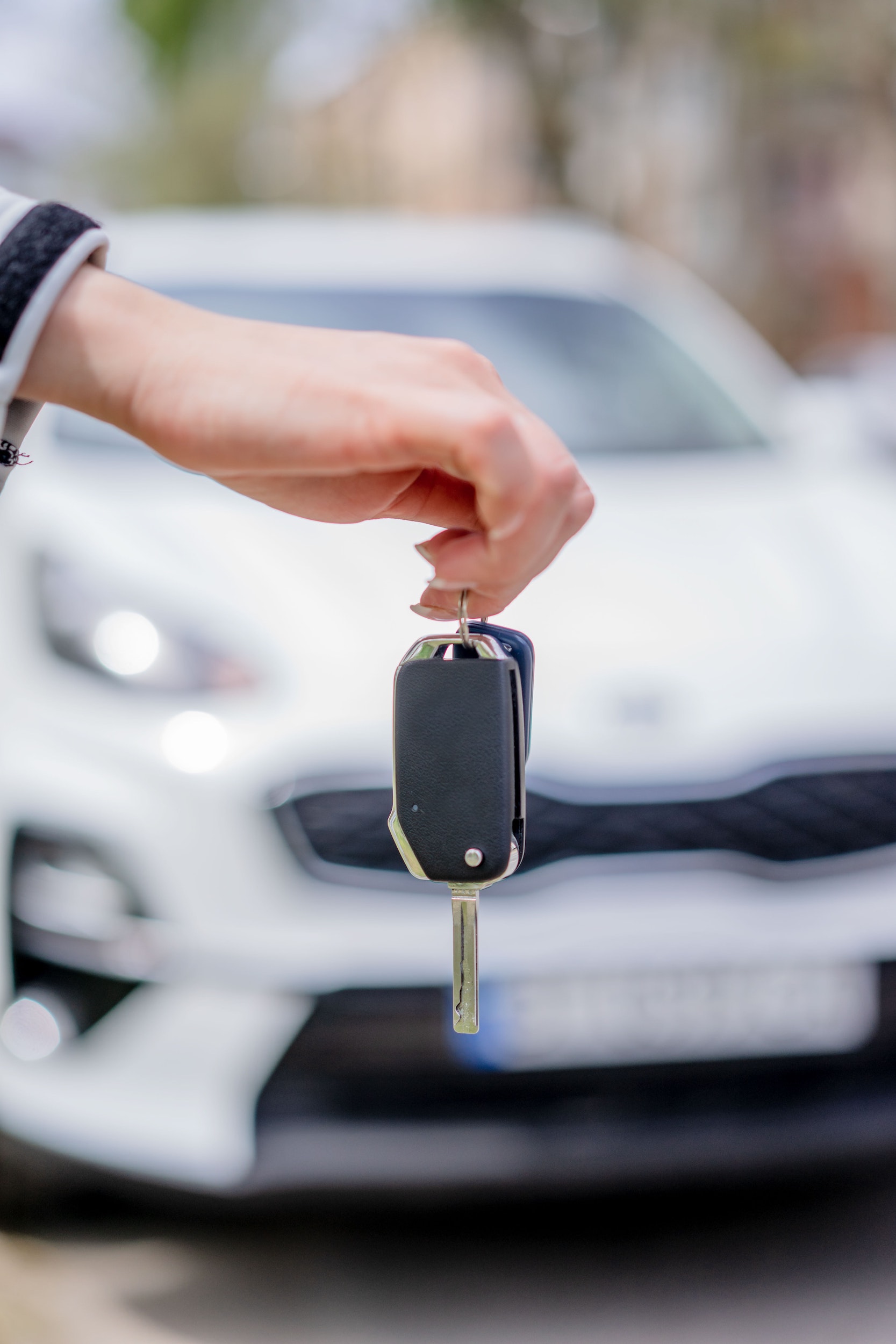 Person holding the keys to a car with the car in the background that has been blurred